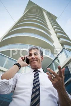 Low Angle View Of Caucasian Businessman Using Cell Phone At High Rise Building