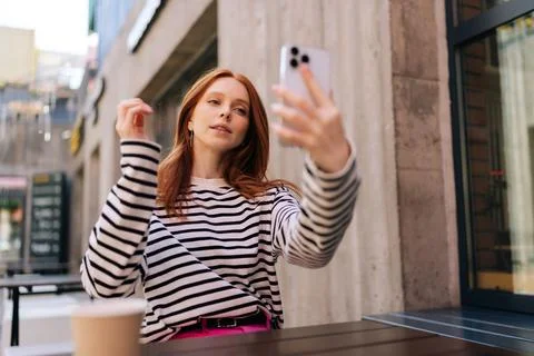 Low-angle view of charming redhead female tourist making selfie or video call to Stock Photos