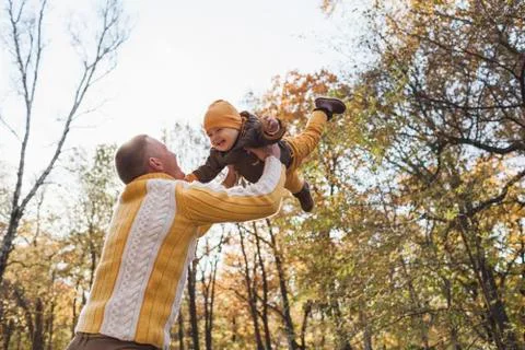 Low angle view of cheerful man lifting baby boy at park during autumn Fotos de archivo