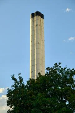 Low angle view of a chimney surrounded by trees against blue sky at sunset. Foto stock