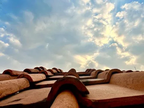 Low Angle View of Clay Roof Tiles Against Blue Sky with Clouds and Sunlight Stock Photos