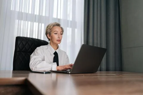 Low-angle view of concentrated elegant middle-aged business woman sitting in Stock Photos