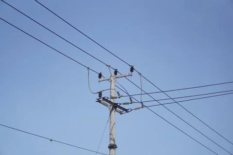 Low-angle view of a concrete utility pole with power transmission lines against Stock Photos