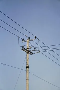 Low-angle view of a concrete utility pole with power transmission lines against Stock Photos
