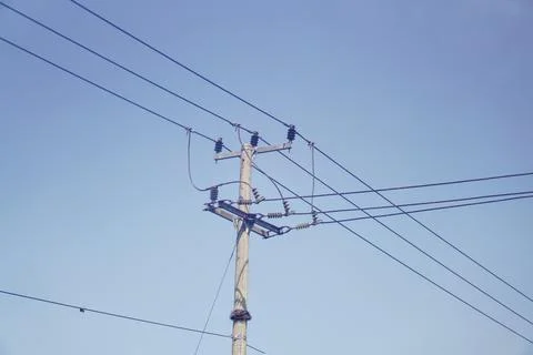 Low-angle view of a concrete utility pole with power transmission lines against Stock Photos