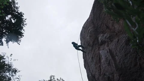 A low-angle view of a daring sports girl rappelling down a big rock amidst .. Video stock 329294247