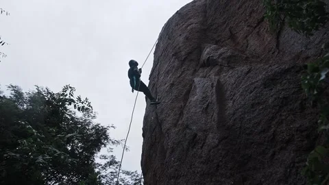 A low-angle view of a daring sports girl rappelling down a big rock amidst .. Video stock 329294261
