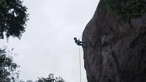 A low-angle view of a daring sports girl rappelling down a big rock amidst .. Video stock 329294262