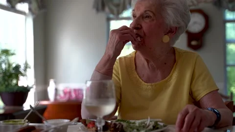 Low angle view of elderly woman in dining room eating with a glass of wine in a Video stock 136426049