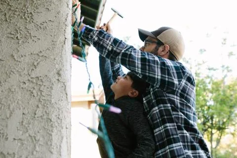 Low angle view of father with son hanging string lights on wall during Christmas Foto stock