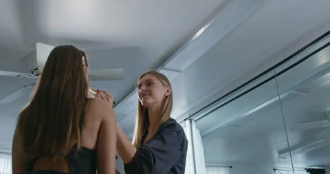 A low-angle view of a female makeup artist applying makeup to a client in a Vidéo 324820225