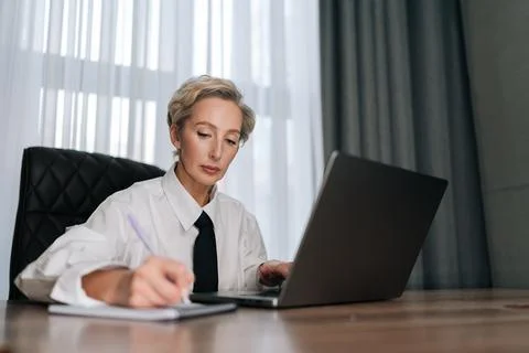 Low-angle view of focused middle-aged business woman using laptop computer for Stock Photos