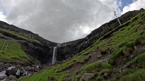 Low angle view of Fossa waterfall with tourist standing by stream, Faroe Islands Stock Footage 339713095