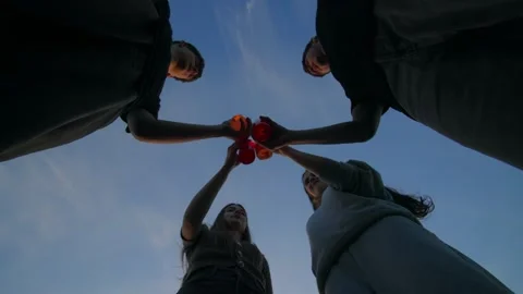 Low angle view of four teenagers clinking glass bottles against a blue sky. Stock-Footage 335818830