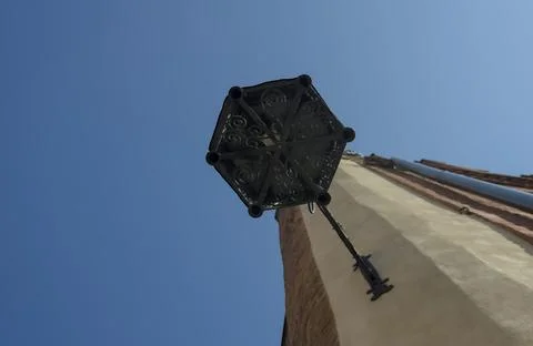 Low-angle view of geometric black forged lantern, blue sky, church tower. Stock Photos