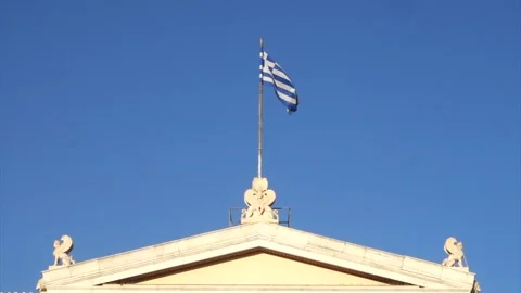 Low angle view of Greek flag waving atop classical building under clear blue sky Video stock 312664279