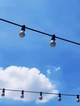 Low Angle View of Hanging Electric Light Bulbs Against Cloudy Sky Foto stock