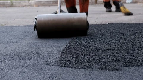 Low angle view of a heavy hand roller flattening fresh hot black asphalt Stock-Footage 339801912