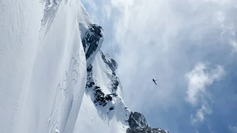LOW ANGLE VIEW: Helicopter flies over snowy peaks and skier starts riding down Stock Footage 229046401