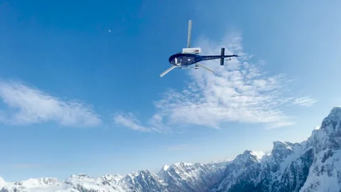LOW ANGLE VIEW: Helicopter takes off after dropping off snowboarders and skiers Stock Footage 229038596