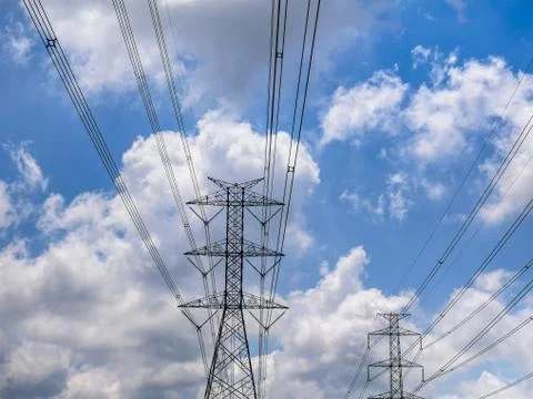 Low Angle View of High Voltage Tower and Power Lines Against Blue Cloudy Sky Foto stock