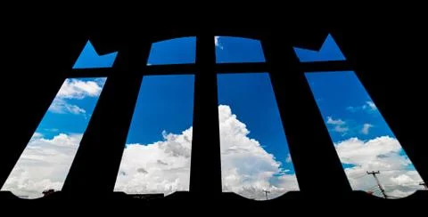 Low angle view of h=white cotton clouds against silhouetted window frame. Stock Photos