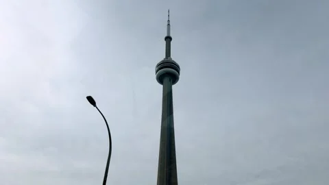 Low-angle view of the iconic CN Tower piercing a dense overcast sky in Toronto. Vidéo 343681003