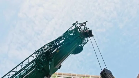 Low-angle view of a large green crane arm lowering its hook. Industrial Stock Footage 337957474