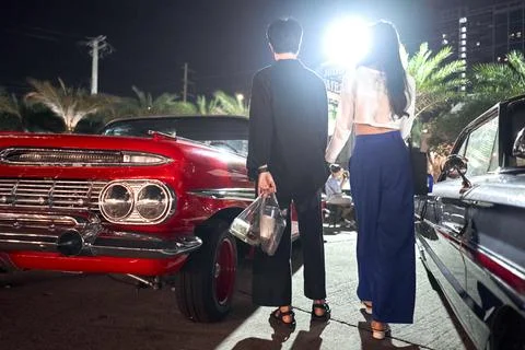 Low angle view of a lesbian couple standing among vintage cars in a night fair Stock Photos