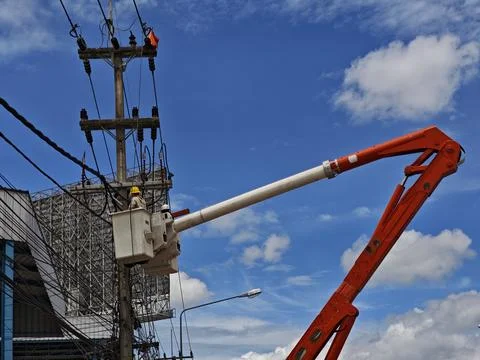 Low angle view of lineman workers in bucket truck with orange boom arm. Stock Photos