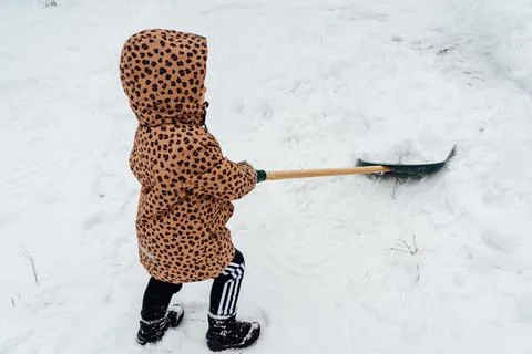 Low angle view of the little kid girl helping to clean pathway from snow with Stock Photos