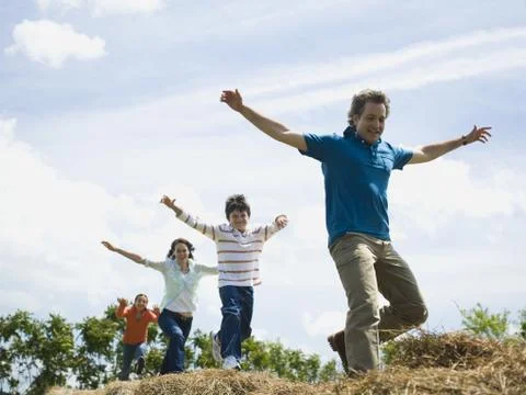 Low angle view of a man and a woman jumping with their children on hay bales Foto stock