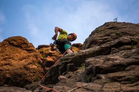 Low angle view of a man climbing on cliff against blue sky. Rope, helmet and 스톡 사진