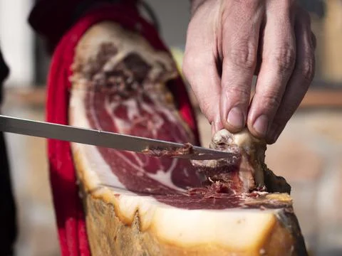 Low angle view of man hand cutting a slice of dried spanish jamon serrano. Stock Photos