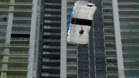 Low-Angle View Of A Man As He Parachutes Past A Modern Highrise Building - Stockbeeldmateriaal 196900275