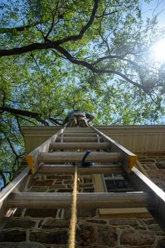 Low angle view of man on a ladder cleaning gutters of a stone house vertical Stock Photos
