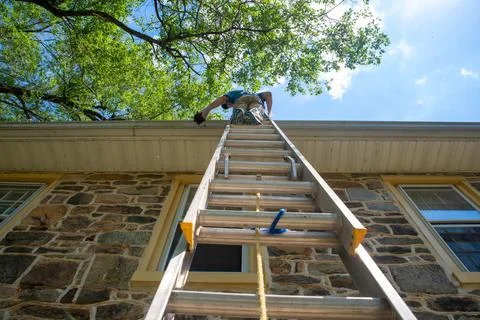 Low angle view of a man on a ladder cleaning gutters of old stone home Stock Photos