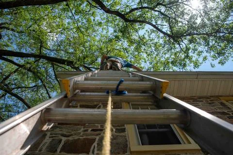 Low angle view of man on ladder cleaning gutters of stone home Stock Photos