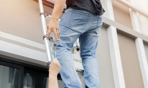 Low angle view of a man on a ladder taking a screwdriver from the assistant. Stock Photos