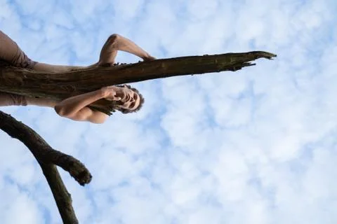 Low angle view of man looking away while lying on log against cloudy sky in Stock Photos