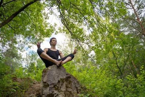 Low angle view of man meditating while sitting on rock against trees in forest Stock Photos
