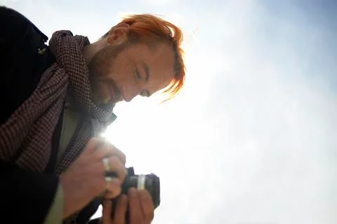 Low angle view of man watching pictures on DSLR camera against sky 库存照片