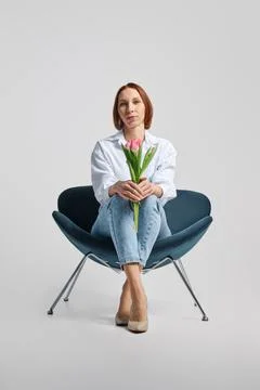 Low angle view at middle aged positive woman sitting in armchair with tulips Foto stock