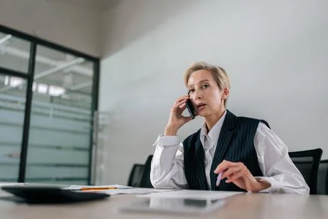 Low-angle view of middle-aged businesswoman making business call sitting on Stock Photos