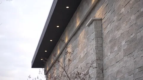 Low-angle view of a modern building's stone facade illuminated by warm soffit Video stock 321189658