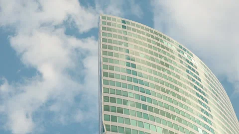 Low-angle view of a modern glass skyscraper with a curved facade reflecting a br Stock Footage 338027315