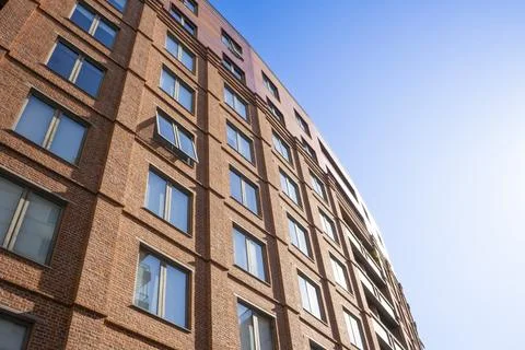Low angle view of modern red brick residential building facade against blue s Stock Photos