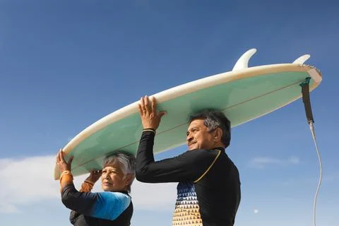 Low angle view of multiracial senior couple carrying surfboard over heads Fotos Stock