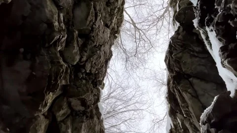 Low angle view of a narrow rock crevice with bare winter trees and light snowfal Stock Footage 325478010