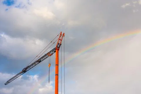 Low angle view of an orange construction crane under a cloudy sky with a rainbow Stock Photos